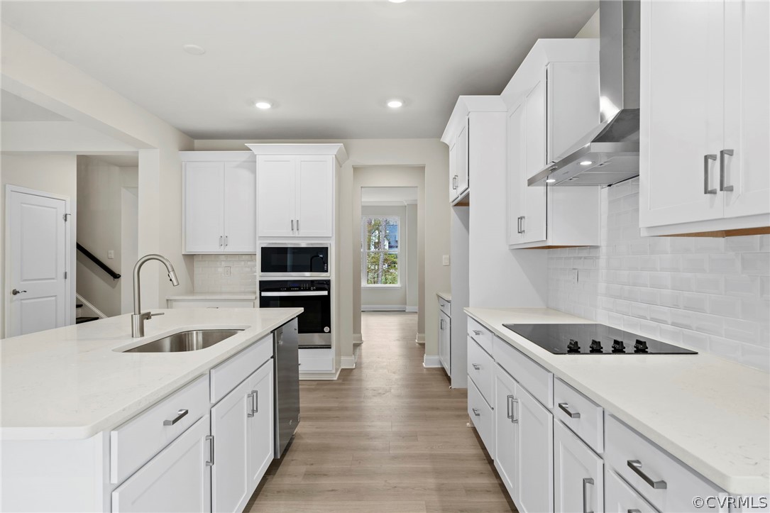 Kitchen featuring stainless steel appliances, backsplash, sink, light wood-type flooring, and wall chimney range hood