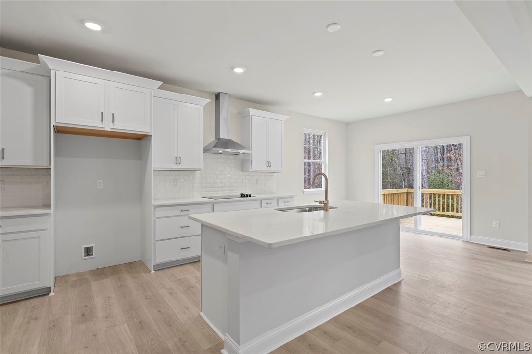 Kitchen featuring sink, tasteful backsplash, light hardwood / wood-style floors, wall chimney range hood, and white cabinetry