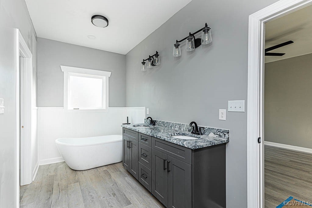 Bathroom featuring hardwood / wood-style floors, a bathing tub, double sink vanity, and ceiling fan