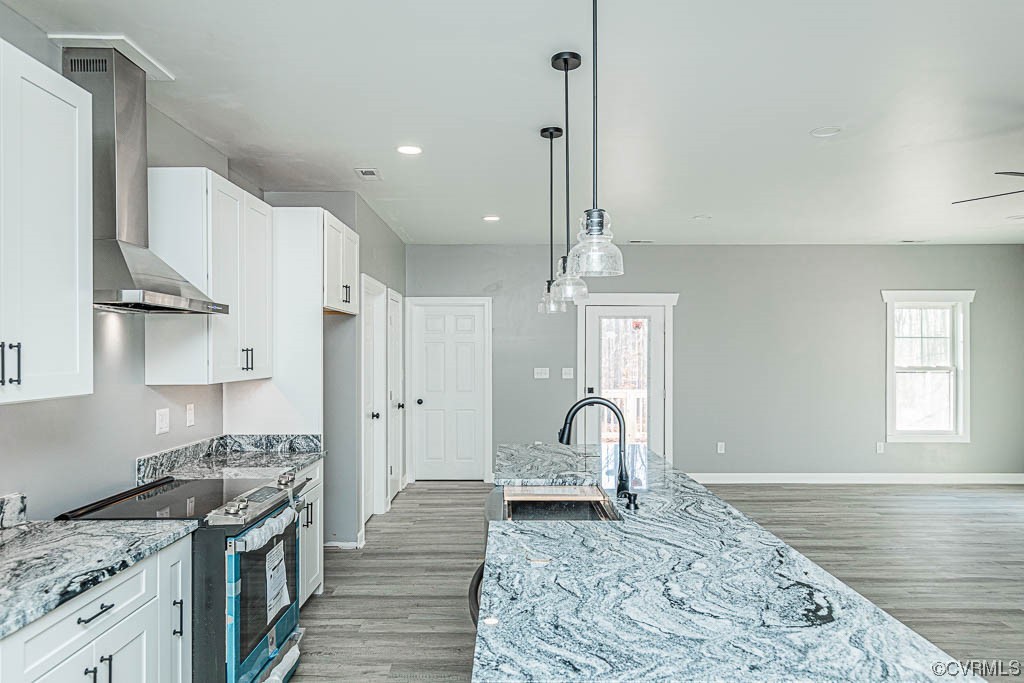Kitchen featuring wall chimney range hood, light hardwood / wood-style floors, sink, decorative light fixtures, and electric range