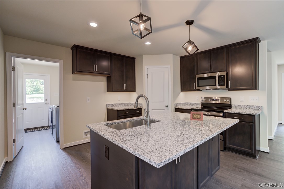 Kitchen with dark wood-type flooring, hanging light fixtures, sink, and appliances with stainless steel finishes