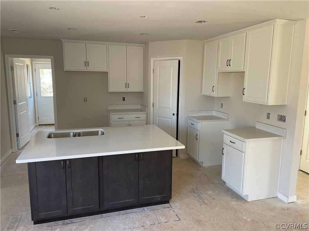 Kitchen featuring white cabinets, a center island with sink, and sink