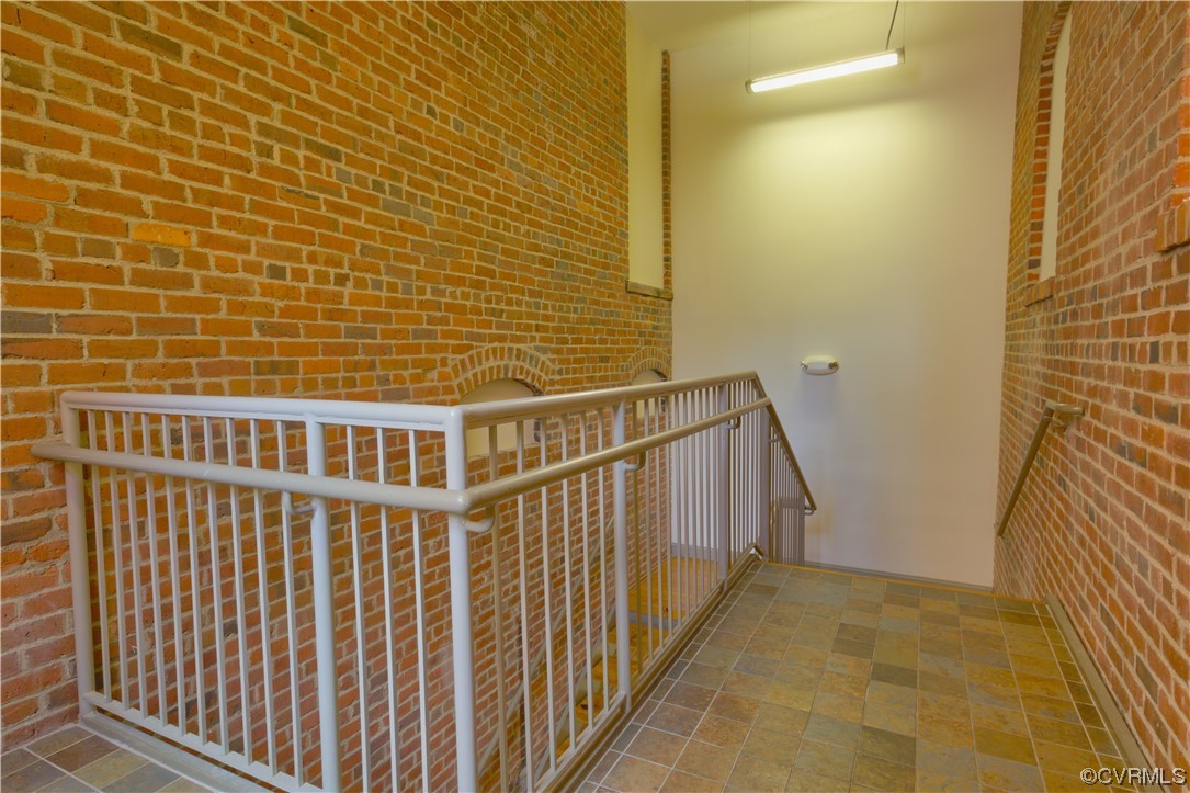 Staircase featuring brick wall and light tile floors