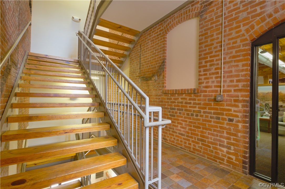 Staircase with dark tile flooring and brick wall