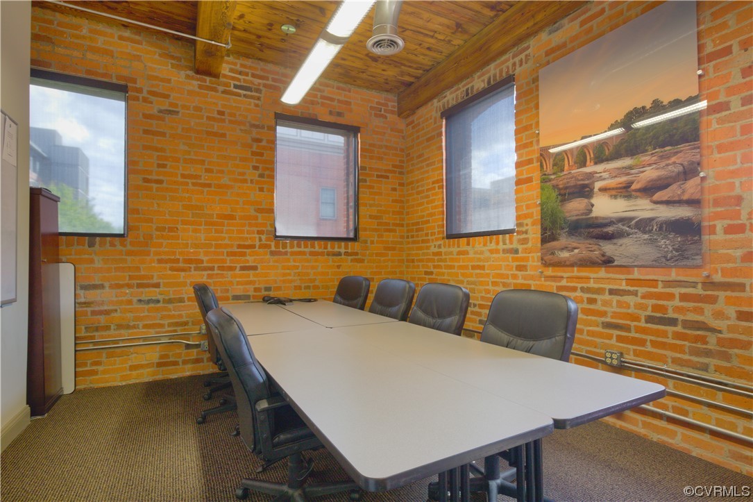 Office area with dark colored carpet, wooden ceiling, and brick wall