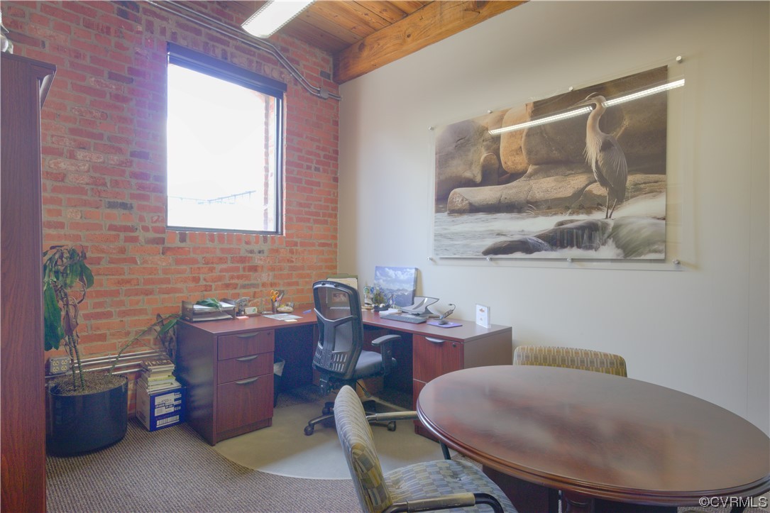 Office featuring light carpet, wood ceiling, and brick wall