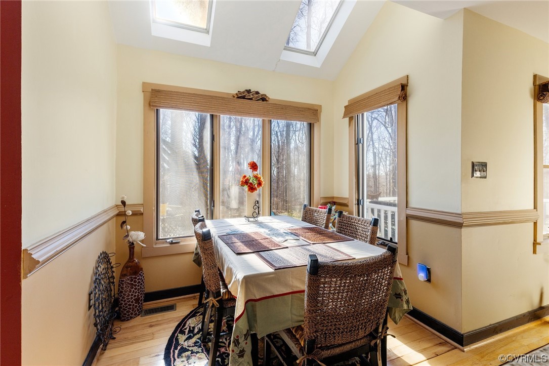 Dining room with light hardwood / wood-style flooring and vaulted ceiling with skylight