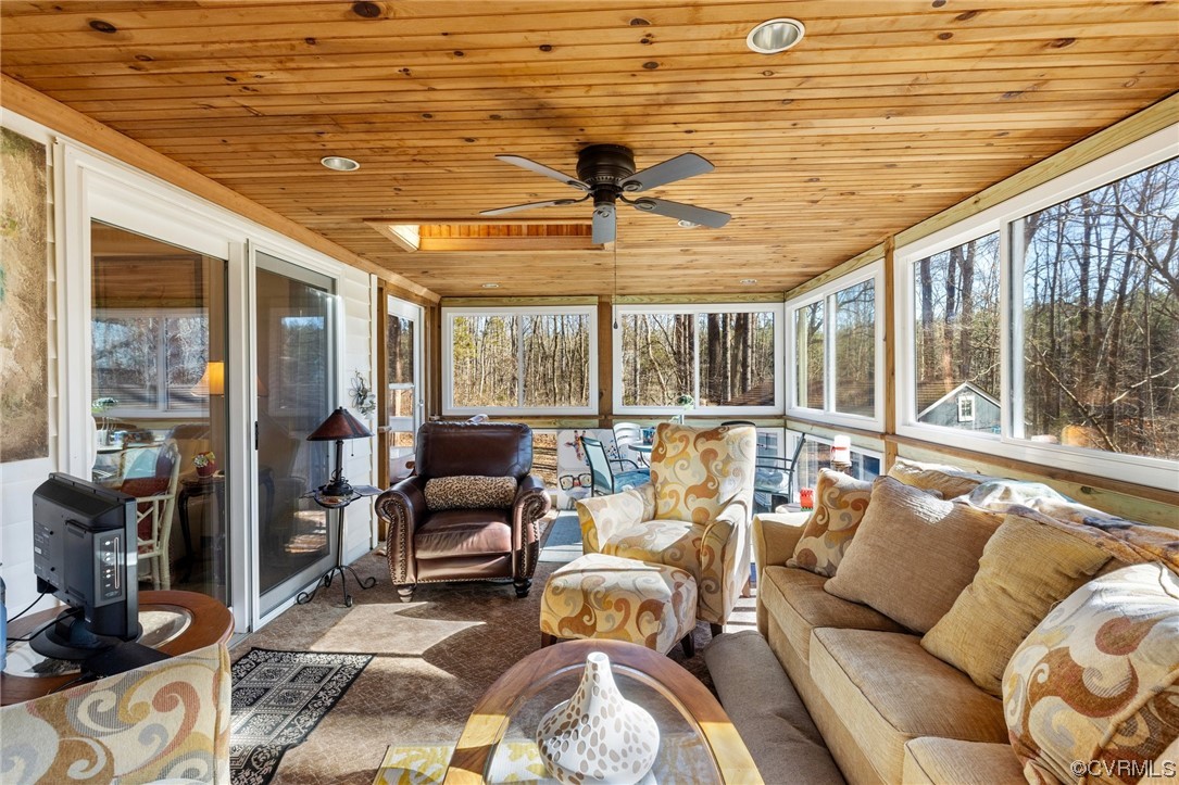 Sunroom / solarium featuring a wood stove, wood ceiling, ceiling fan, and a skylight