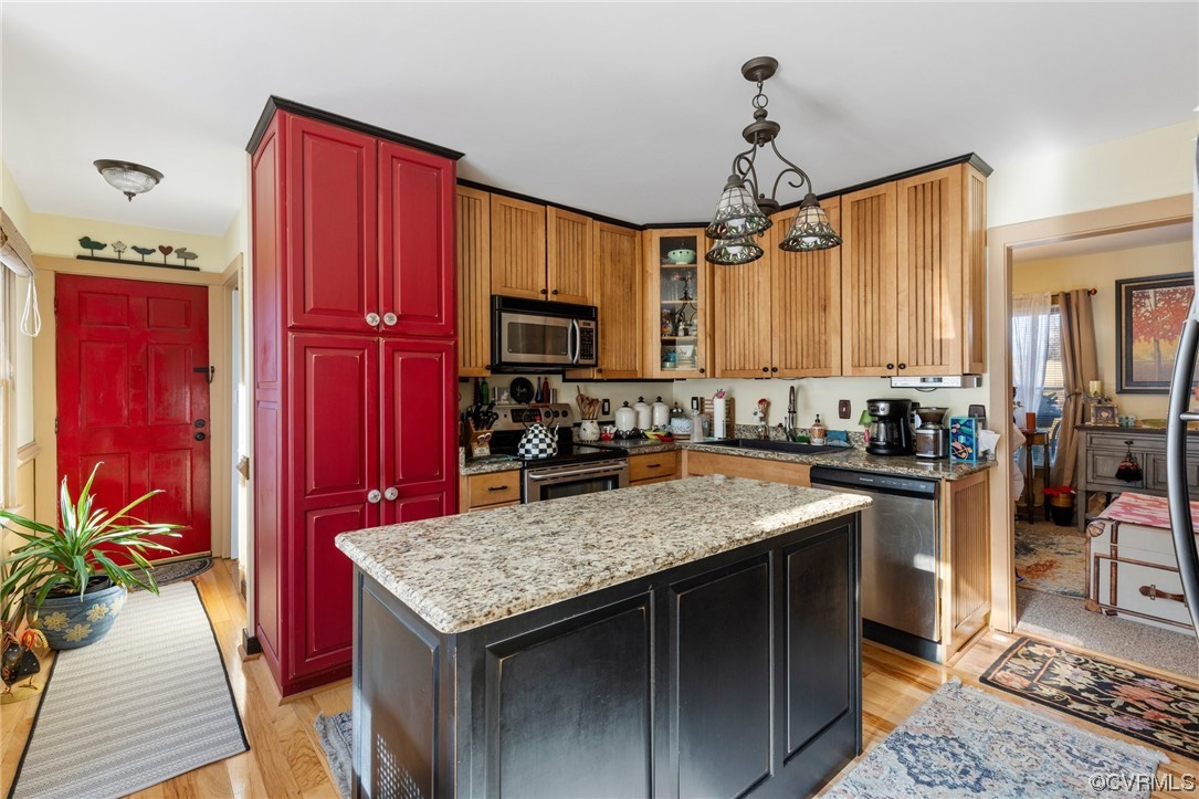 Kitchen featuring pendant lighting, stainless steel appliances, light stone countertops, light hardwood / wood-style floors, and a center island