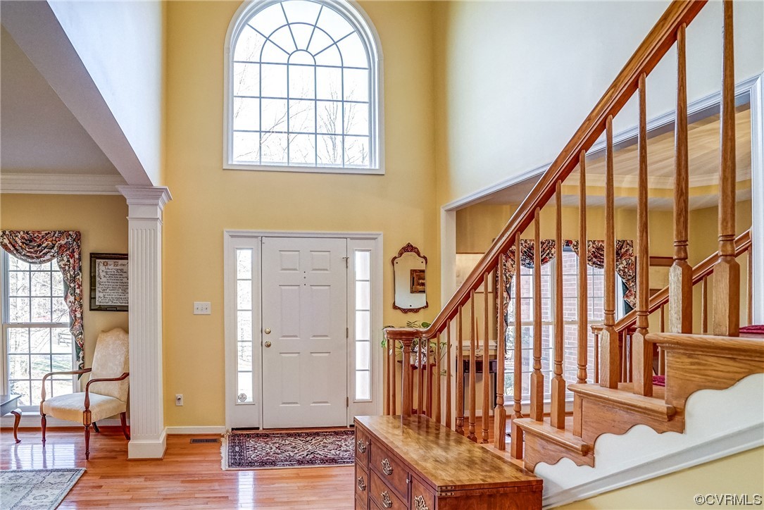 Entrance foyer featuring plenty of natural light, light hardwood / wood-style floors, crown molding, and decorative columns