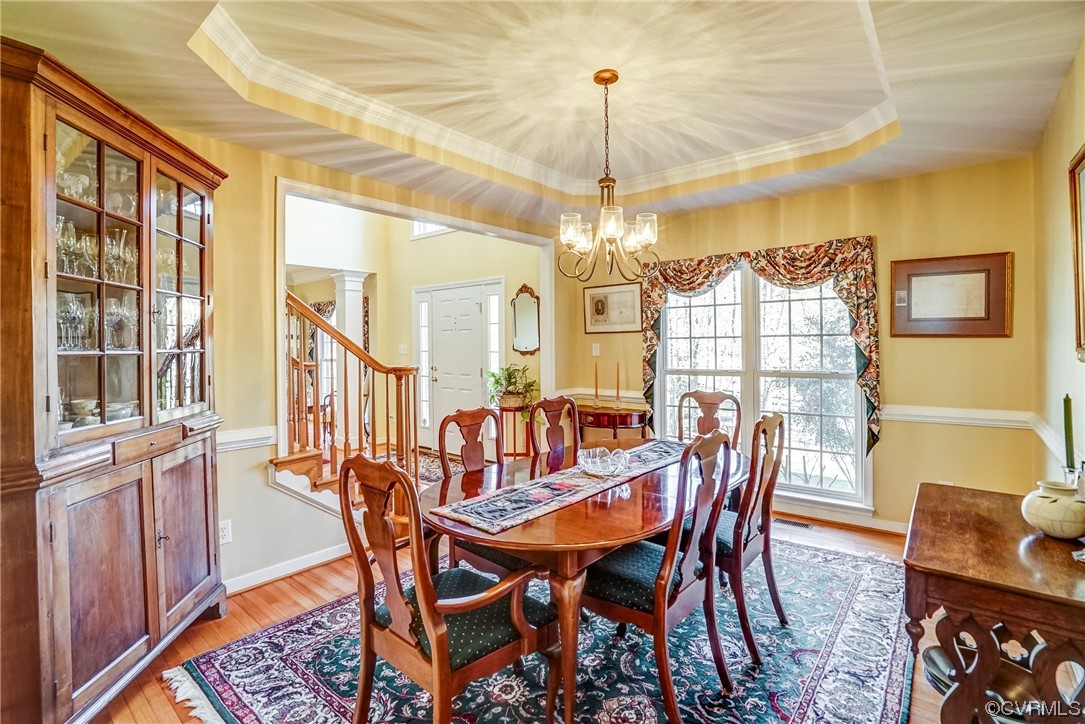 Dining space featuring light hardwood / wood-style floors, ornate columns, crown molding, an inviting chandelier, and a tray ceiling