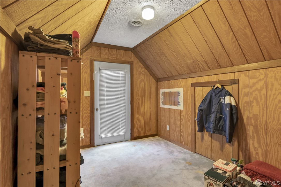 Bonus room with wood walls, light colored carpet, a textured ceiling, and lofted ceiling