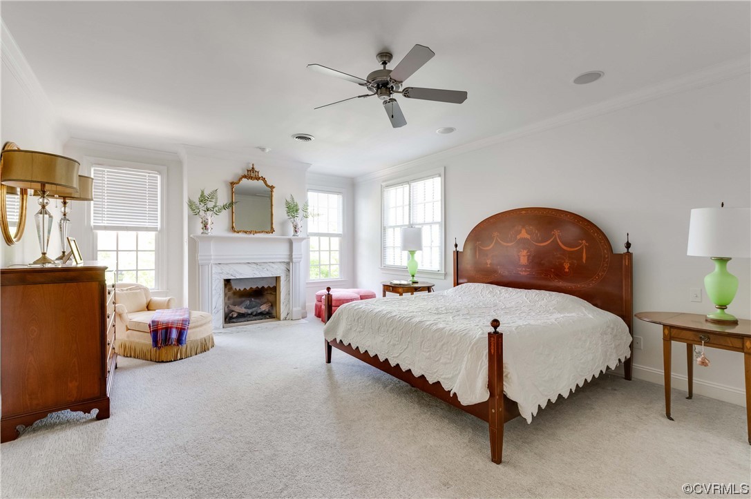 Carpeted bedroom featuring a high end fireplace, crown molding, multiple windows, and ceiling fan