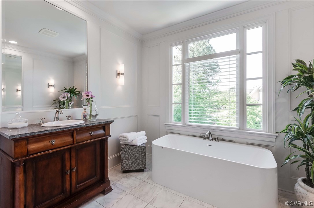 Bathroom with ornamental molding, tile floors, vanity, and a bath