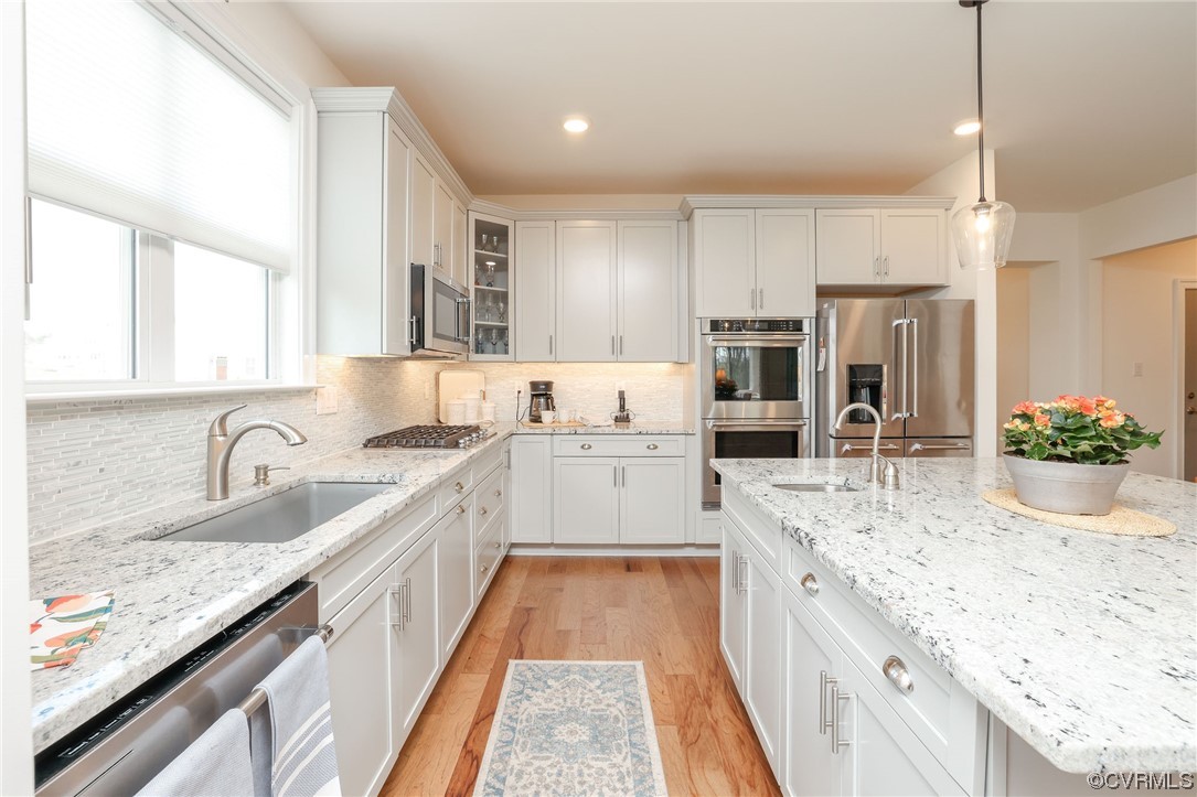 Kitchen with sink, backsplash, stainless steel appliances, and light hardwood / wood-style floors