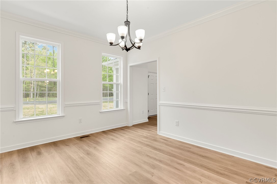 Spare room with a chandelier, a healthy amount of sunlight, light hardwood / wood-style flooring, and ornamental molding