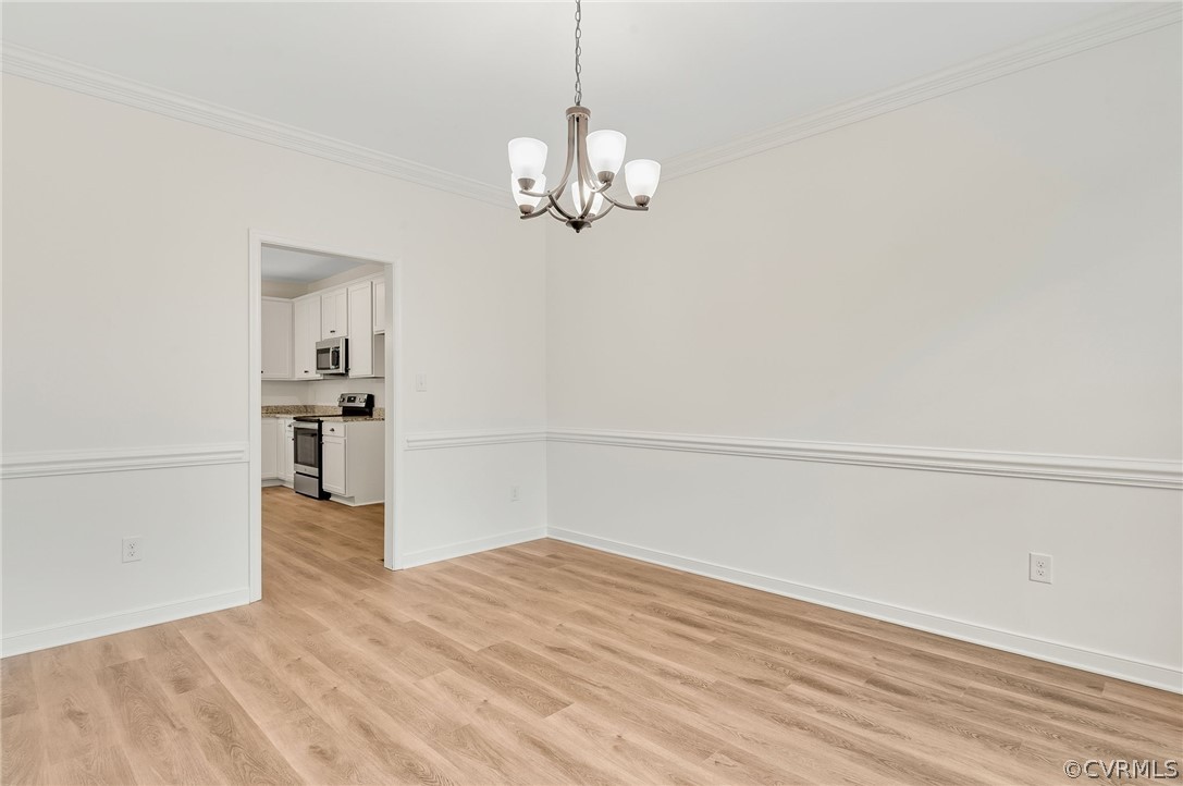 Empty room featuring ornamental molding, a notable chandelier, and light hardwood / wood-style flooring