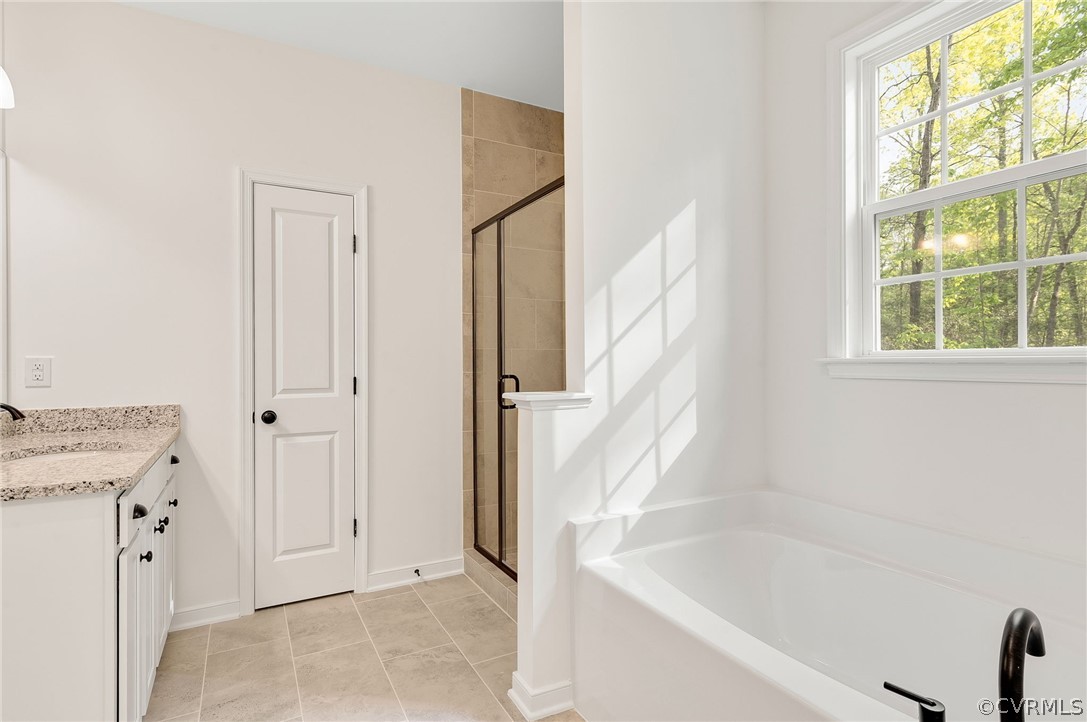 Bathroom with a healthy amount of sunlight, separate shower and tub, tile floors, and vanity
