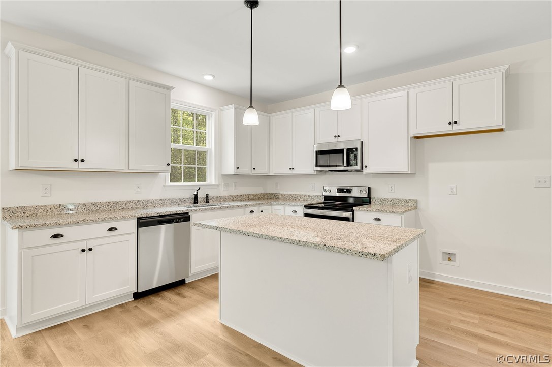 Kitchen featuring a kitchen island, light hardwood / wood-style flooring, stainless steel appliances, white cabinetry, and pendant lighting