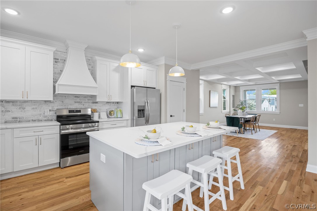 Kitchen with appliances with stainless steel finishes, a center island, coffered ceiling, light hardwood / wood-style flooring, and premium range hood