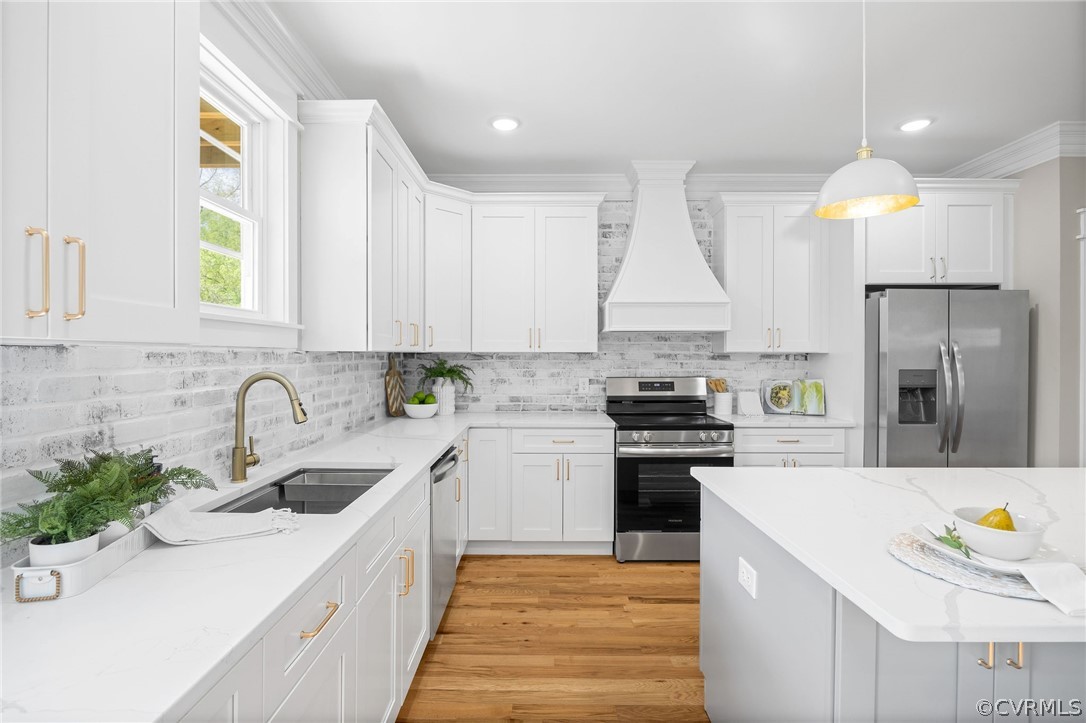 Kitchen featuring sink, decorative light fixtures, stainless steel appliances, light hardwood / wood-style flooring, and custom range hood