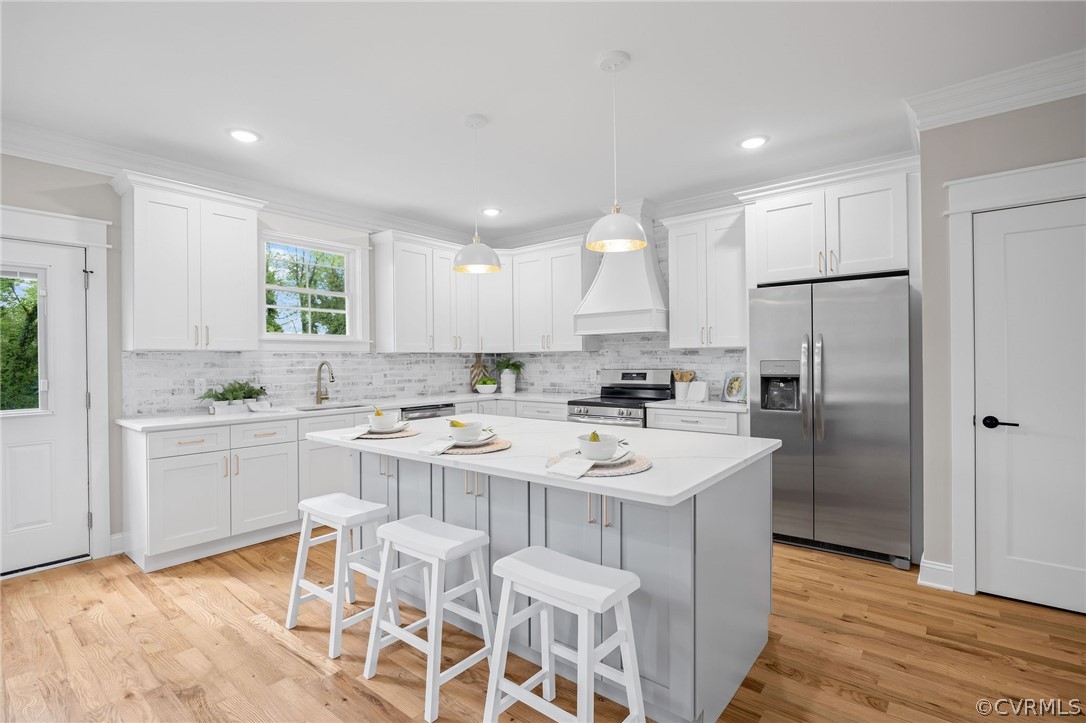 Kitchen featuring appliances with stainless steel finishes, light hardwood / wood-style flooring, a kitchen island, premium range hood, and a breakfast bar