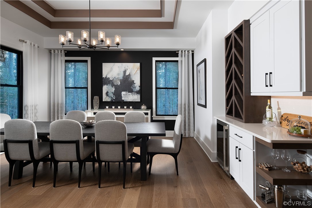 Dining space featuring wine cooler, hardwood / wood-style flooring, an inviting chandelier, and a tray ceiling
