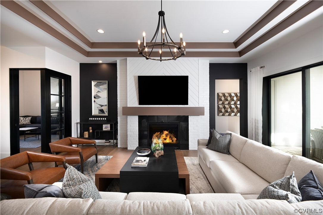Living room featuring an inviting chandelier, a raised ceiling, hardwood / wood-style flooring, and a brick fireplace