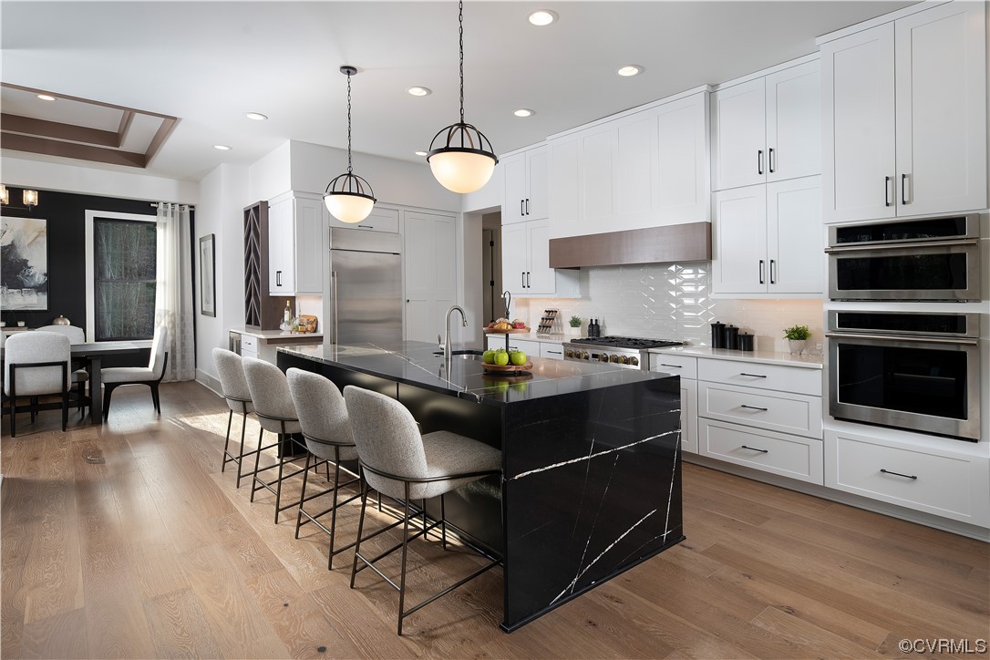 Kitchen featuring wood-type flooring, stainless steel appliances, a breakfast bar area, hanging light fixtures, and an island with sink