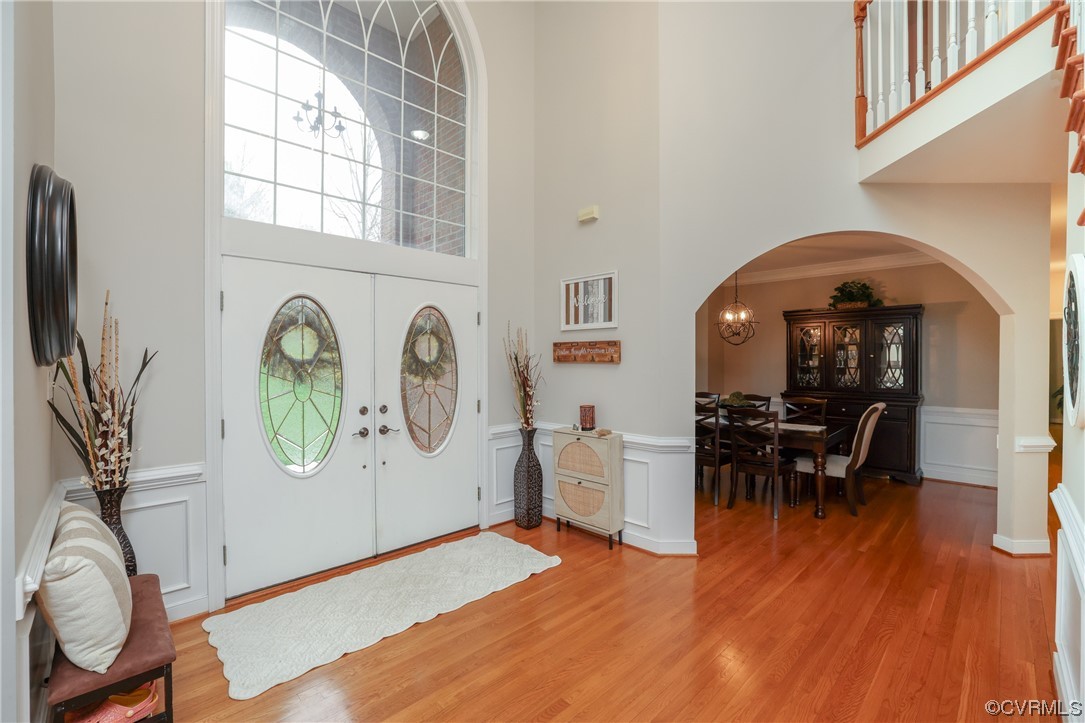 Open foyer with cathedral ceiling, hardwood floors, arched doorways, and decorative trim