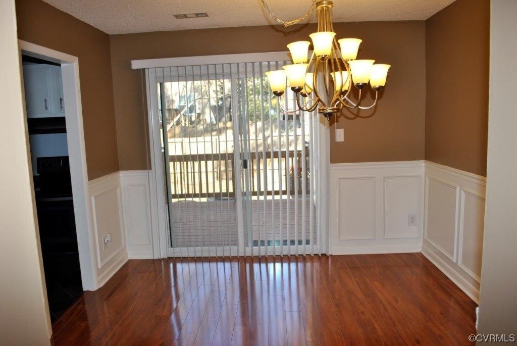 Unfurnished dining area with an inviting chandelier, dark hardwood / wood-style flooring, and a textured ceiling
