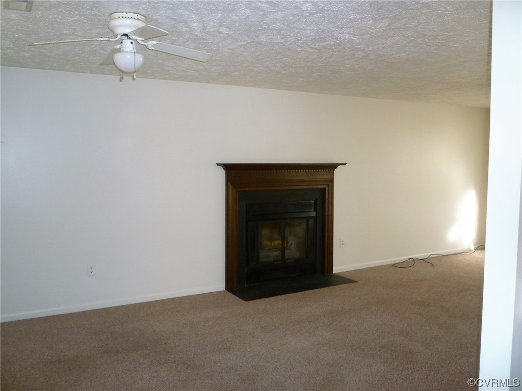 Unfurnished living room with dark colored carpet, a textured ceiling, and ceiling fan