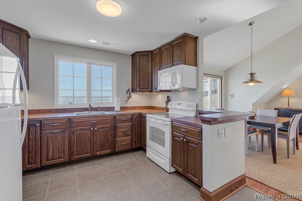 Kitchen with sink, white appliances, decorative light fixtures, light tile floors, and plenty of natural light