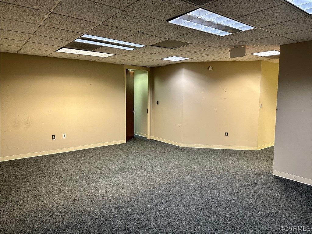 Unfurnished room featuring dark colored carpet and a drop ceiling