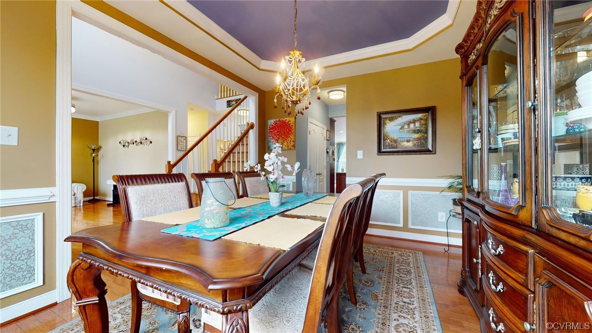 Dining room with a notable chandelier, ornamental molding, a tray ceiling, and wood flooring
