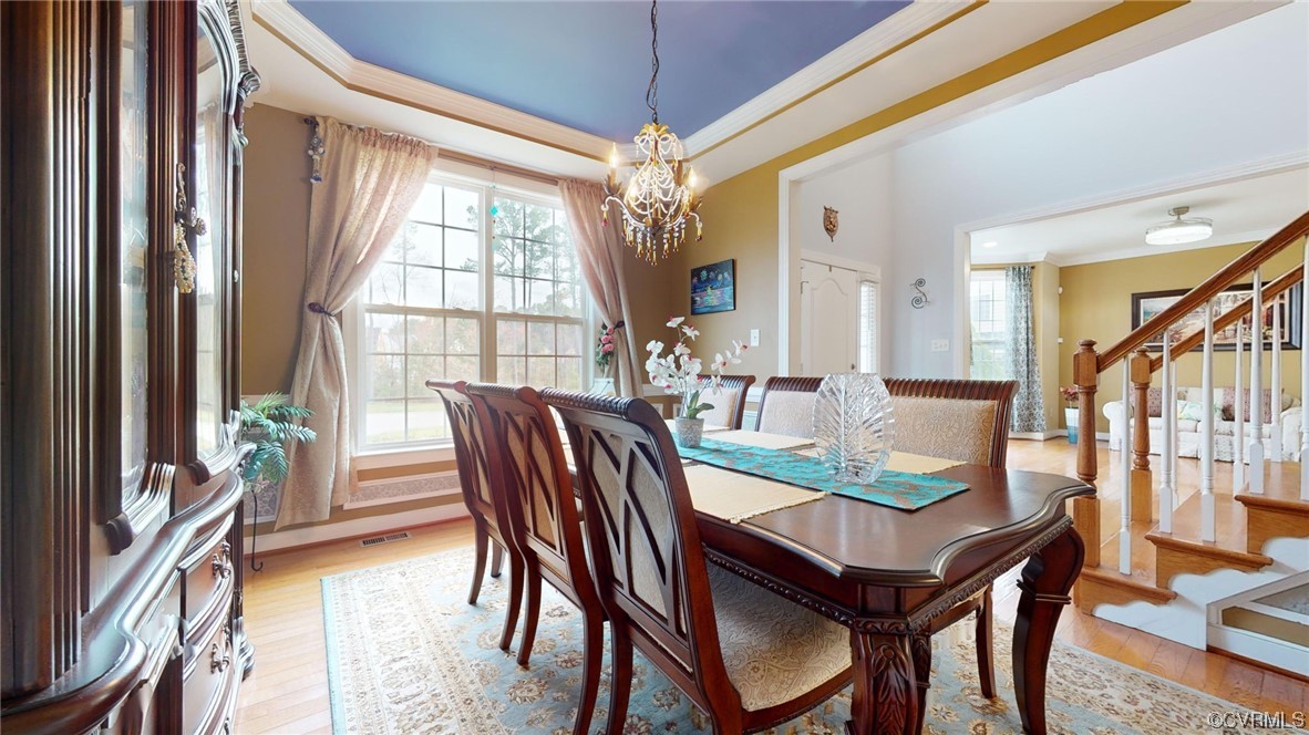 Dining area featuring an inviting chandelier, ornamental molding, a tray ceiling, and light hardwood  wood floors
