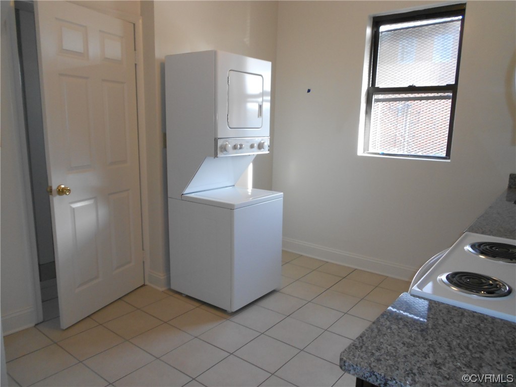 Washroom with light tile flooring and stacked washer and clothes dryer