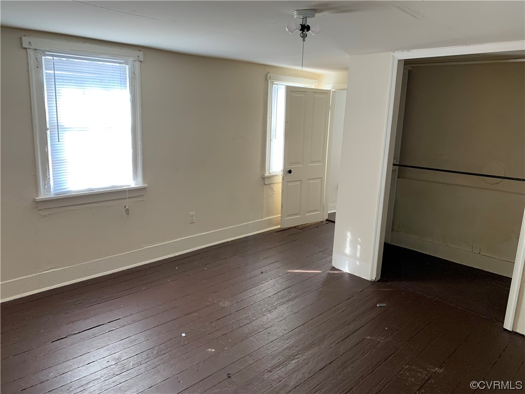 Unfurnished bedroom featuring dark wood-type flooring, multiple windows, a closet, and ceiling fan