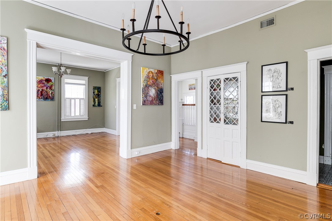 Foyer with an inviting chandelier, ornamental molding, and light wood-type flooring