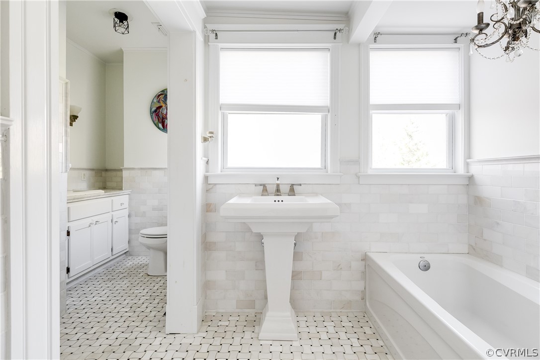 En-Suite Bathroom featuring a bath, toilet, tile flooring, and tile walls