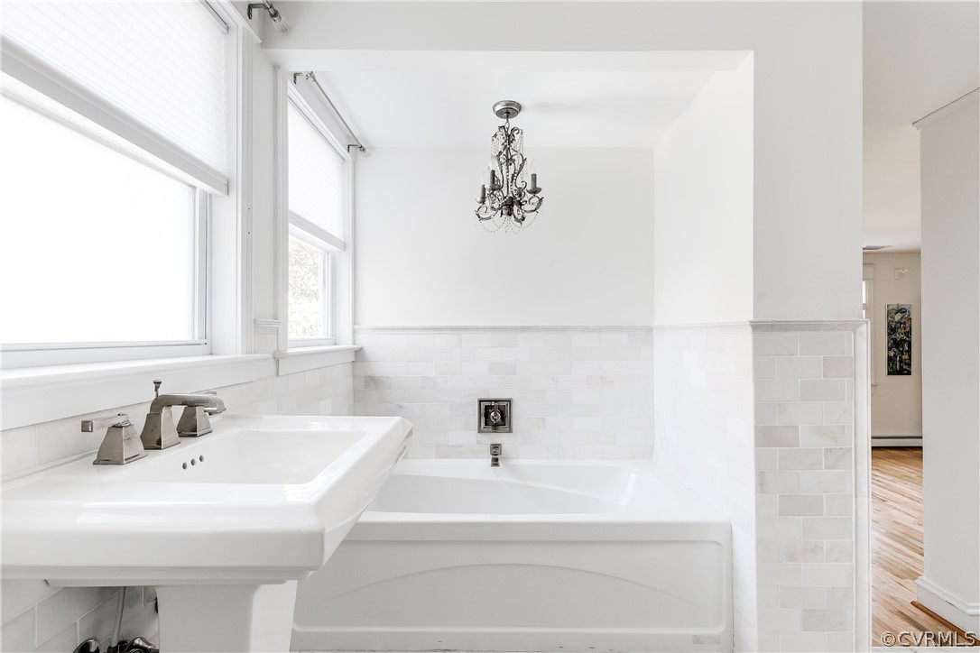 En-Suite Bathroom featuring a tub, an inviting chandelier, a baseboard heating unit, and wood-type flooring