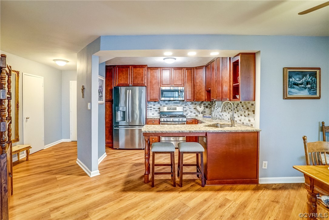 Kitchen with appliances with stainless steel finishes, backsplash, light wood-type flooring, and sink