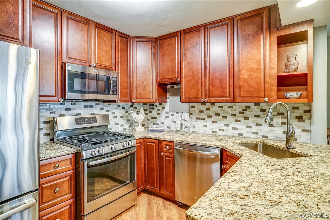 Kitchen featuring appliances with stainless steel finishes, light hardwood / wood-style flooring, tasteful backsplash, and sink
