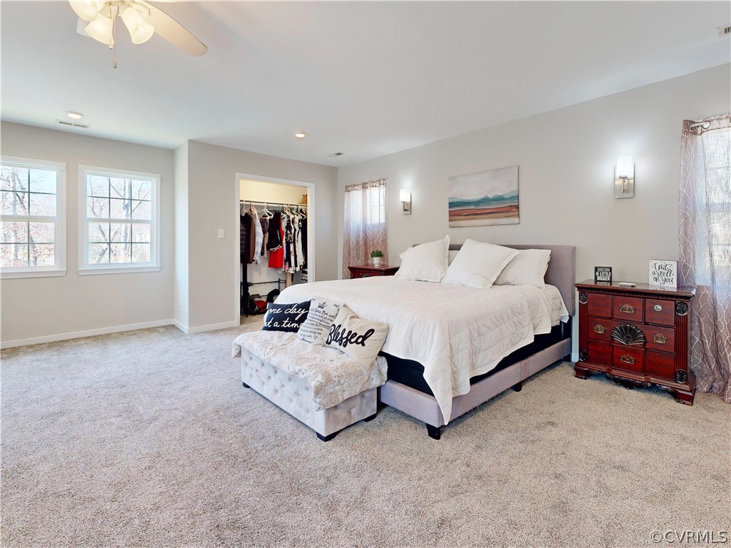 Bedroom with a spacious closet, multiple windows, light colored carpet, and ceiling fan