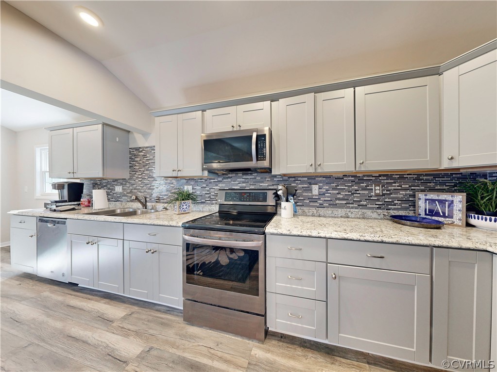 Kitchen featuring tasteful backsplash, stainless steel appliances, light hardwood / wood-style floors, sink, and lofted ceiling