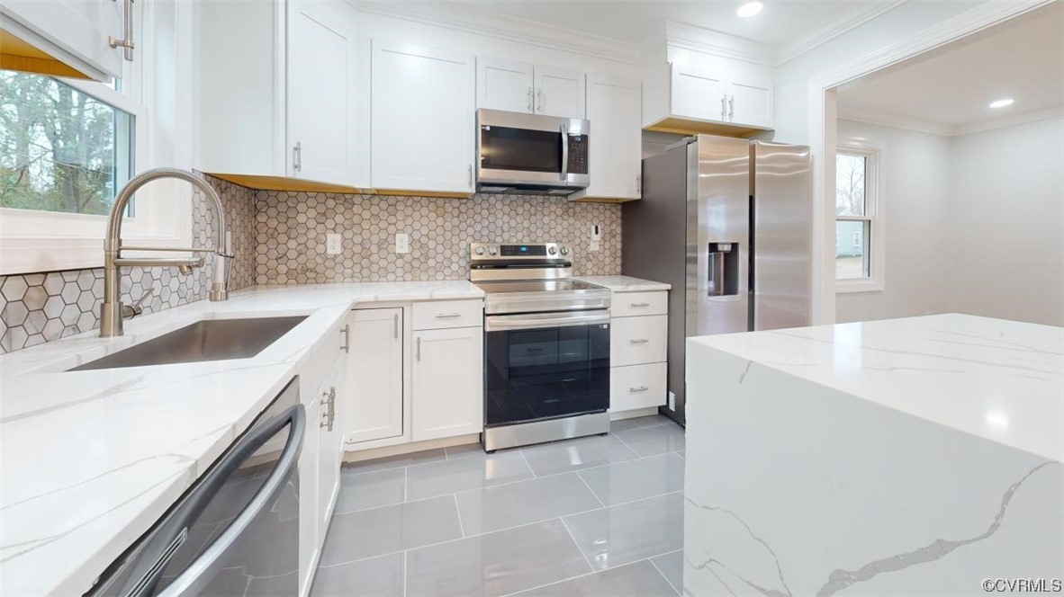 Kitchen with appliances with stainless steel finishes, white cabinetry, and light stone counters