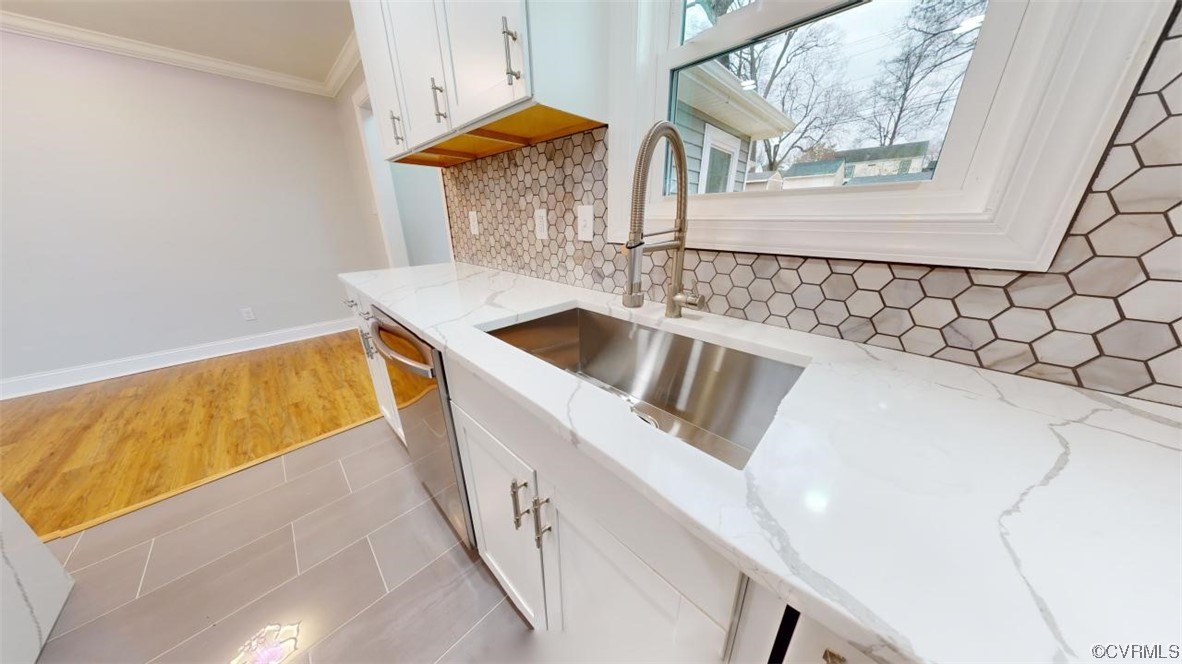 Kitchen with white cabinetry, tasteful backsplash, light hardwood / wood-style floors, stainless steel dishwasher, and light stone counters