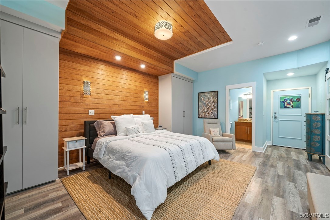 Bedroom featuring ensuite bathroom, wood walls, wood ceiling, and light hardwood / wood-style floors