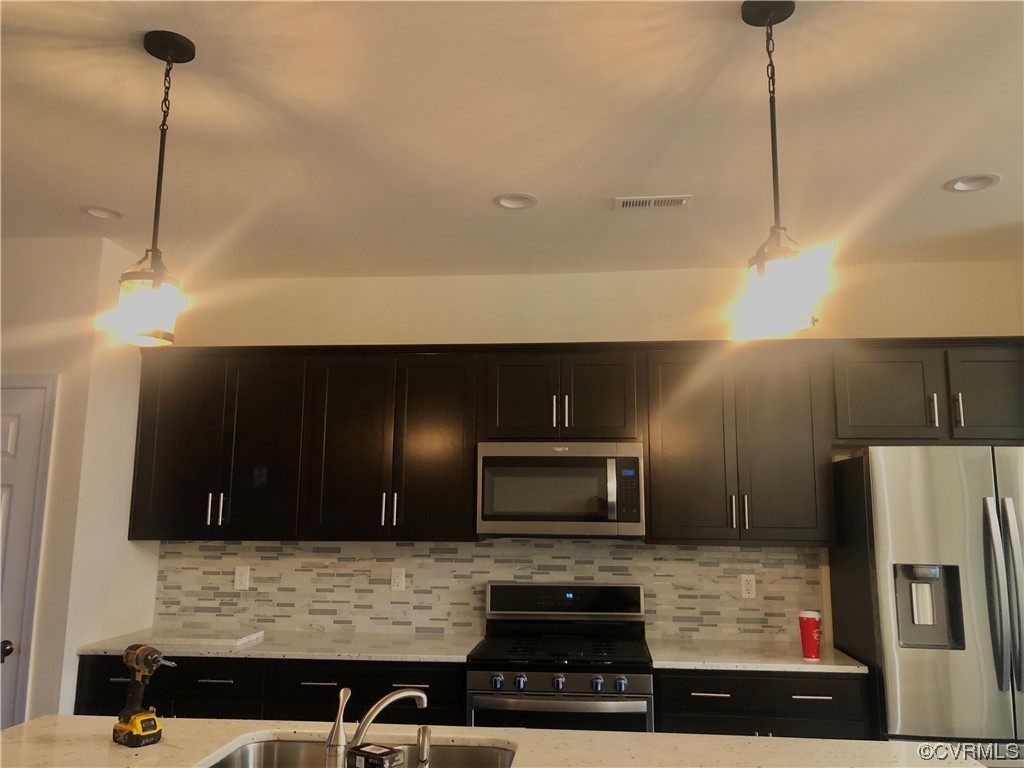 Kitchen featuring appliances with stainless steel finishes, backsplash, pendant lighting, and sink