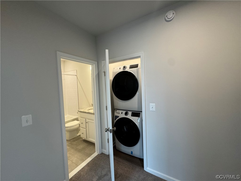 Laundry room with stacked washer and dryer and dark colored carpet